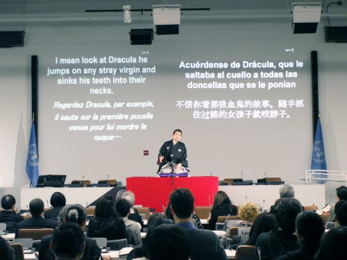 公演を行う桂小春團治さん。スクリーンには各国語の字幕が表示された＝２月19日、マンハッタン区の国連本部（©Live Act International）
