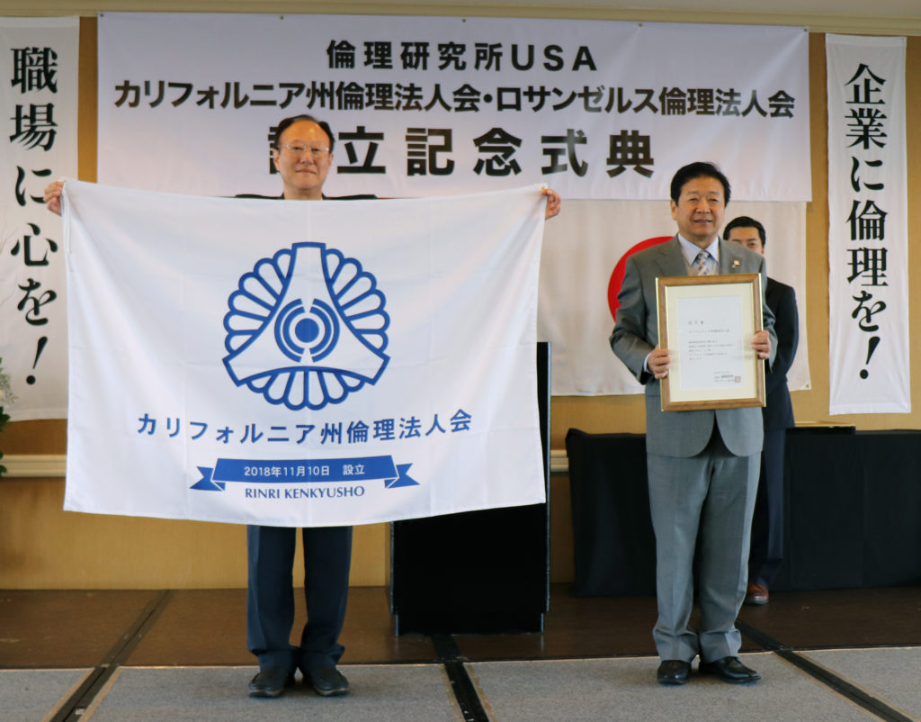 カリフォルニア倫理法人会の設立の認可書と行動旗の授与。右は同会長・飯田隆氏